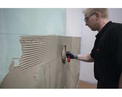 Artisan appliquant de la colle à carrelage sur une plaque de plâtre avec une spatule dentée
