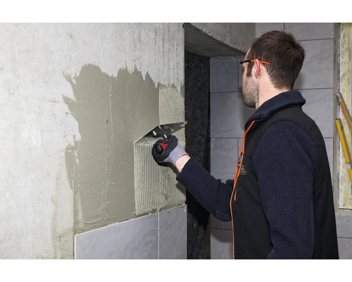 Artisan appliquant de la colle à carrelage sur un mur à l'aide d'une truelle dentée pour la pose de carrelage.