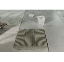 Pose de carrelage avec colle à carrelage appliquée et un seau sur une chape