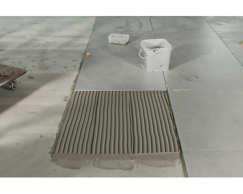 Pose de carrelage avec colle à carrelage appliquée et un seau sur une chape