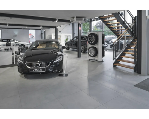 Concessionnaire Volvo moderne avec véhicules d'exposition, présentoir de pneus et un escalier dans un espace de vente spacieux avec carrelage.