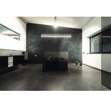 Salle de bains moderne avec baignoire îlot, murs foncés, carrelage au sol grand format et éclairage LED indirect.