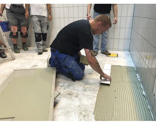 Artisan pose des carreaux de sol sur un lit de colle à carrelage dans une pièce carrelée.