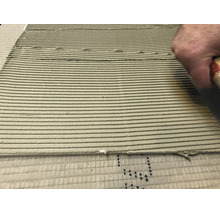 Main appliquant de la colle à carrelage avec une spatule crantée sur le support pour la pose de carrelage