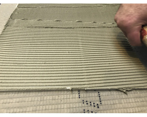 Main appliquant de la colle à carrelage avec une spatule crantée sur le support pour la pose de carrelage