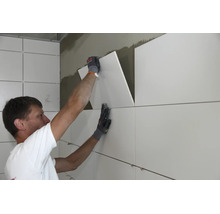 Artisan posant de grands carreaux sur un mur intérieur avec de la colle à carrelage.