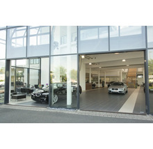 Façade en verre moderne d une concession automobile avec deux véhicules exposés et un escalier à l intérieur.