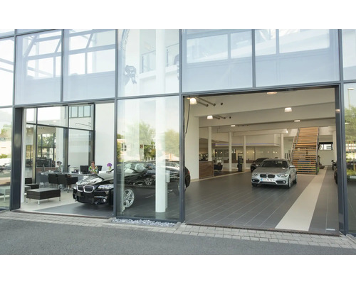 Façade en verre moderne d une concession automobile avec deux véhicules exposés et un escalier à l intérieur.