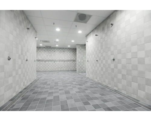 Salle de douche spacieuse et carrelée avec plusieurs douches murales, poignées de maintien et caniveaux d'écoulement, design moderne et fonctionnel.