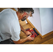 Un artisan fixe des plinthes au mur à l'aide d'une cloueuse sans fil Einhell.