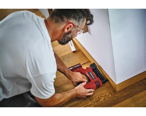 Un artisan fixe des plinthes au mur à l'aide d'une cloueuse sans fil Einhell.