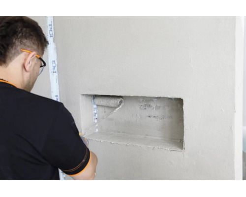 Artisan appliquant de la sous couche avec un rouleau dans une niche murale avec du ruban adhésif PCI