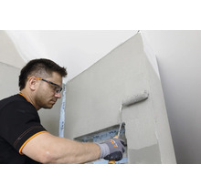 Artisan portant des lunettes de protection et des gants applique une sous couche sur un mur intérieur à l aide d un rouleau à peinture.