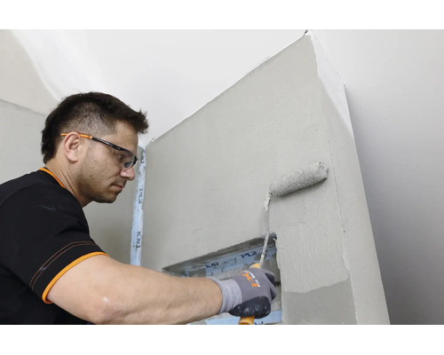 Artisan portant des lunettes de protection et des gants applique une sous couche sur un mur intérieur à l aide d un rouleau à peinture.