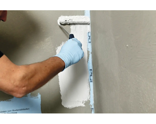 Une personne applique un revêtement d etanchéité liquide sur un mur à l aide d un rouleau pour le rendre imperméable.