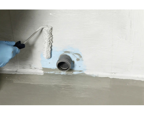 Une personne portant des gants applique un produit d'étanchéité autour d'un tuyau mural avec un rouleau pour assurer l'imperméabilisation.