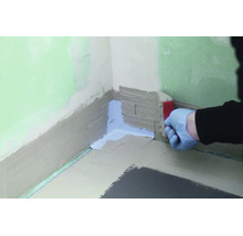 Main avec gant appliquant une bande d etancheite dans un angle de mur pour une etancheite sous carrelage.