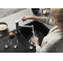 Une personne remplit une carafe en verre avec de l'eau provenant d'un mitigeur de cuisine moderne au-dessus d'un évier encastré noir.
