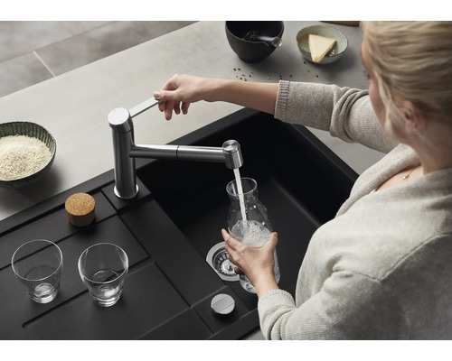 Une personne remplit une carafe en verre avec de l'eau provenant d'un mitigeur de cuisine moderne au-dessus d'un évier encastré noir.