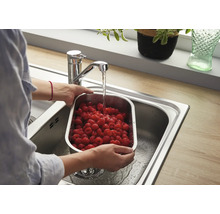 Une personne lave des framboises fraîches dans une passoire en acier inoxydable dans un évier sous un mitigeur monocommande moderne.
