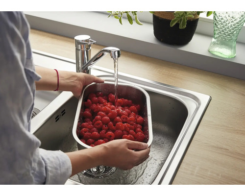 Une personne lave des framboises fraîches dans une passoire en acier inoxydable dans un évier sous un mitigeur monocommande moderne.
