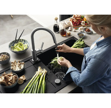Une personne lave des légumes dans un évier encastrable noir moderne avec mitigeur de cuisine extractible dans une cuisine organisée.