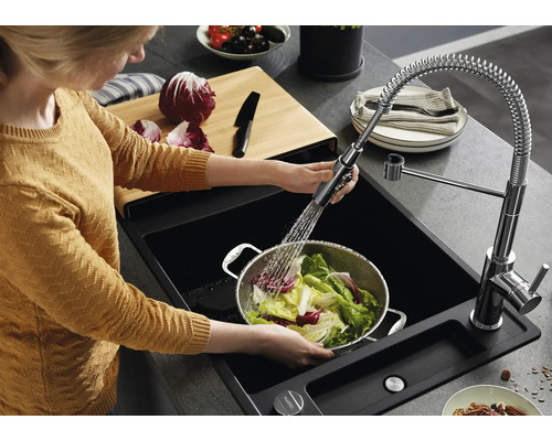 Une personne lave de la salade dans une passoire en métal au-dessus d'un évier noir avec mitigeur de cuisine extractible et ressort en spirale.