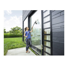 Femme nettoyant une haute façade vitrée sur une maison moderne avec un aspirateur de fenêtre sans fil et kit de rallonge.