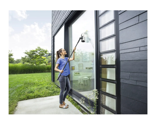 Femme nettoyant une haute façade vitrée sur une maison moderne avec un aspirateur de fenêtre sans fil et kit de rallonge.