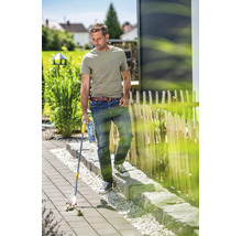Un homme utilise un désherbeur thermique à gaz sur une terrasse pavée pour éliminer les mauvaises herbes entre les dalles.