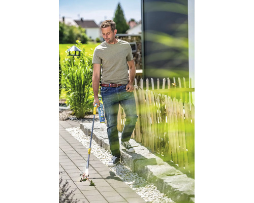 Un homme utilise un désherbeur thermique à gaz sur une terrasse pavée pour éliminer les mauvaises herbes entre les dalles.