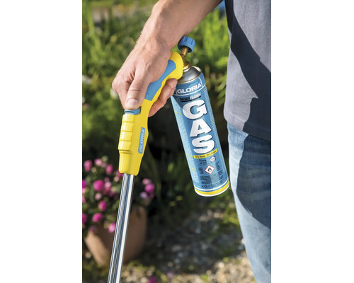 Une personne tient un brûleur thermique à gaz Gloria Thermoflamm avec cartouche de gaz dans un jardin pour le désherbage.
