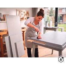 Une femme monte des pièces de mobilier en bois avec un tournevis sur une table de travail dans un atelier lumineux. (Image AI modified or generated)