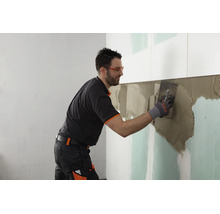 Artisan appliquant de la colle à carrelage sur un mur en plaques de plâtre avec une spatule crantée.