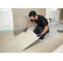 Artisan posant de grands carreaux sur un lit de colle à carrelage préparé dans une salle de bain.
