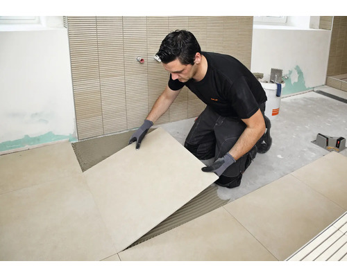 Artisan posant de grands carreaux sur un lit de colle à carrelage préparé dans une salle de bain.