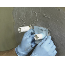 Hand beim Anbringen einer PCI Pecitape Wandmanschette zur Abdichtung einer Rohrdurchführung in einer Wand mit aufgetragener Dichtmasse.