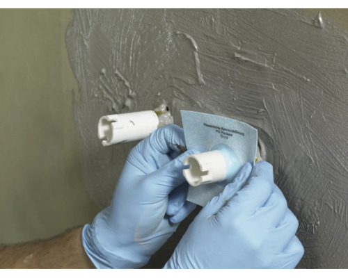 Hand beim Anbringen einer PCI Pecitape Wandmanschette zur Abdichtung einer Rohrdurchführung in einer Wand mit aufgetragener Dichtmasse.