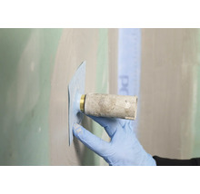Hand mit Schutzhandschuh beim Anbringen einer wasserdichten Dichtmanschette um einen Wandanschluss für Sanitärinstallationen.