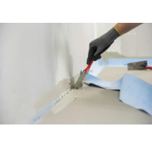Main d un ouvrier portant des gants de protection appliquant du mortier hydrofuge au pinceau sur une jonction mur sol avec une bande d étanchéité