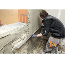 Un artisan égalise l'enduit sur un mur à l'aide d'une règle de maçon.
