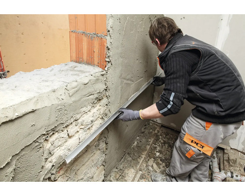 Un artisan égalise l'enduit sur un mur à l'aide d'une règle de maçon.