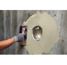 Artisan utilisant une taloche pour reboucher une ouverture murale autour d une traversée de mur encastrée