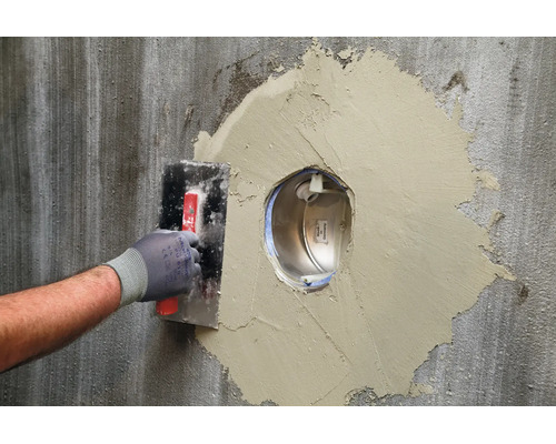 Artisan utilisant une taloche pour reboucher une ouverture murale autour d une traversée de mur encastrée