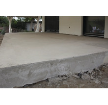 Une terrasse en béton fraîchement coulée devant une maison, la surface est lissée et les bords ne sont pas encore totalement durcis.