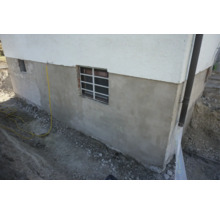 Socle de sous-sol rénové d'une maison avec nouvel enduit extérieur et fenêtre de cave lors de travaux de terrassement.