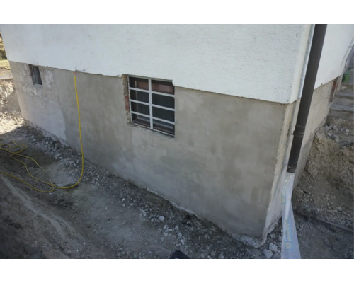 Socle de sous-sol rénové d'une maison avec nouvel enduit extérieur et fenêtre de cave lors de travaux de terrassement.