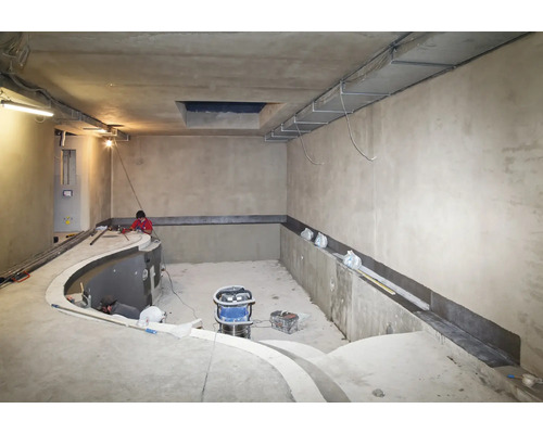 Chantier d une piscine intérieure avec des ouvriers effectuant des travaux d étanchéité sur les murs en béton.