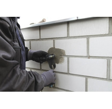 Artisan réparant un joint dans un mur en briques claires avec une truelle à jointoyer.