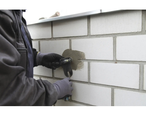 Artisan réparant un joint dans un mur en briques claires avec une truelle à jointoyer.